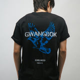 Person wearing a black t-shirt with blue dove bird graphic and white Gwangbok text on the back against a plain background