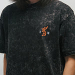 Person wearing a black acid-washed t-shirt with a small graphic of a Korean tiger and 광복 on a plain background