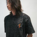 Person wearing a black acid wash t-shirt with a small graphic of an orange Korean tiger and 광복 on a plain background