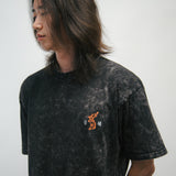 Person wearing a black acid wash t-shirt with a small graphic of an orange Korean tiger and 광복 on a plain background