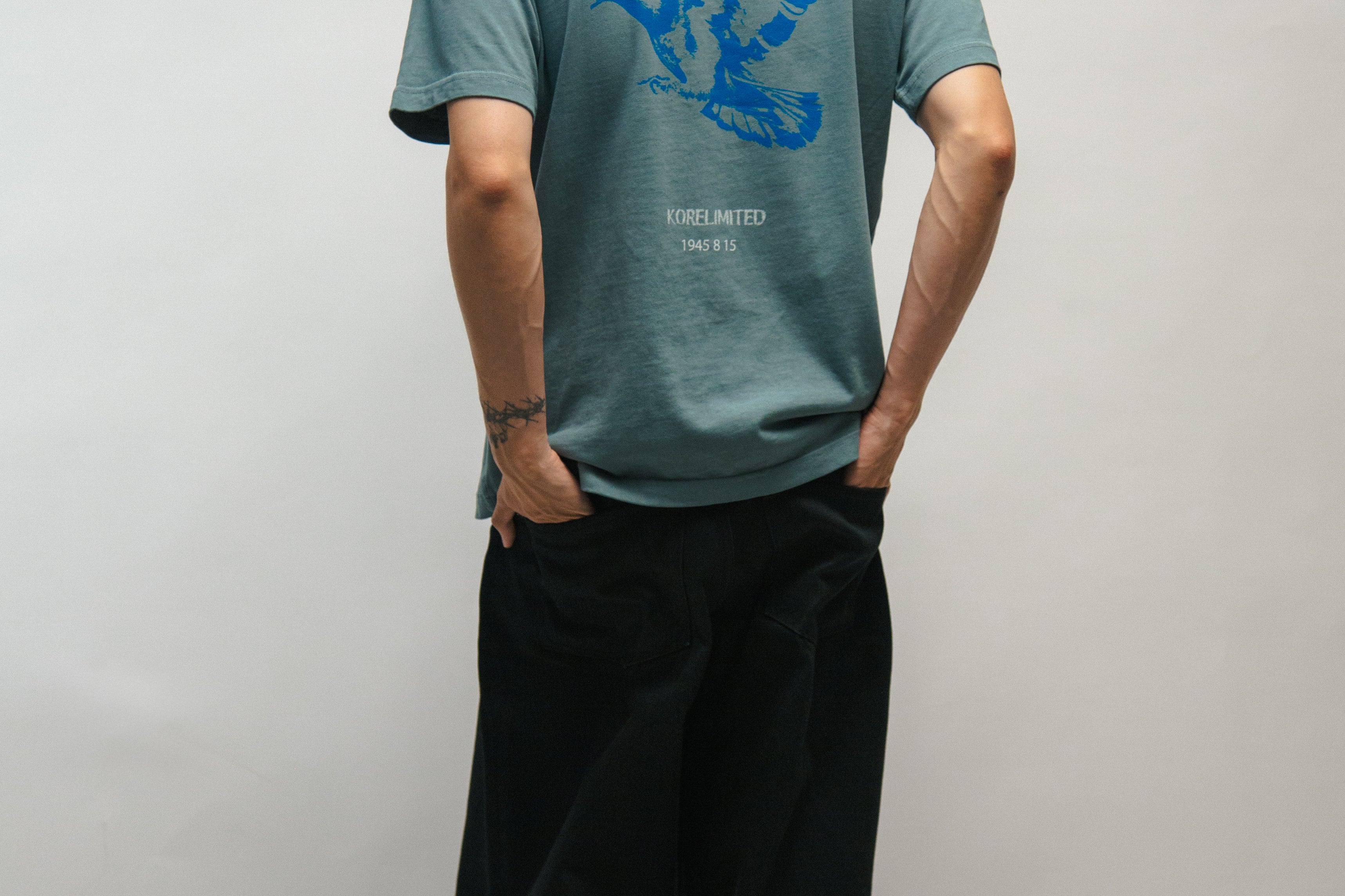 Person wearing a teal t-shirt with blue graphic dove and text Gwangbok on the back, standing against a plain background.