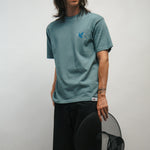 Person wearing a teal t-shirt with a logo of blue dove, holding a black Korean hat called gat against a plain background