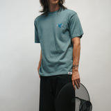 Person wearing a teal t-shirt with a logo of blue dove, holding a black Korean hat called gat against a plain background