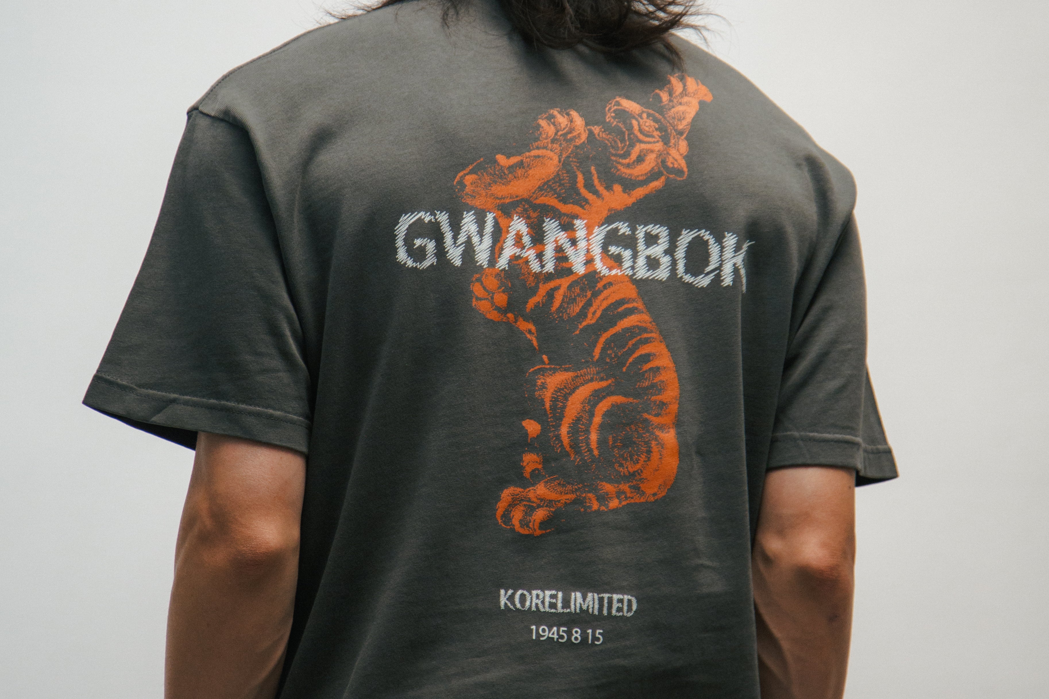 Person wearing a dark gray t-shirt with orange Korean tiger design and text GWANGBOK on the back, against a plain background.