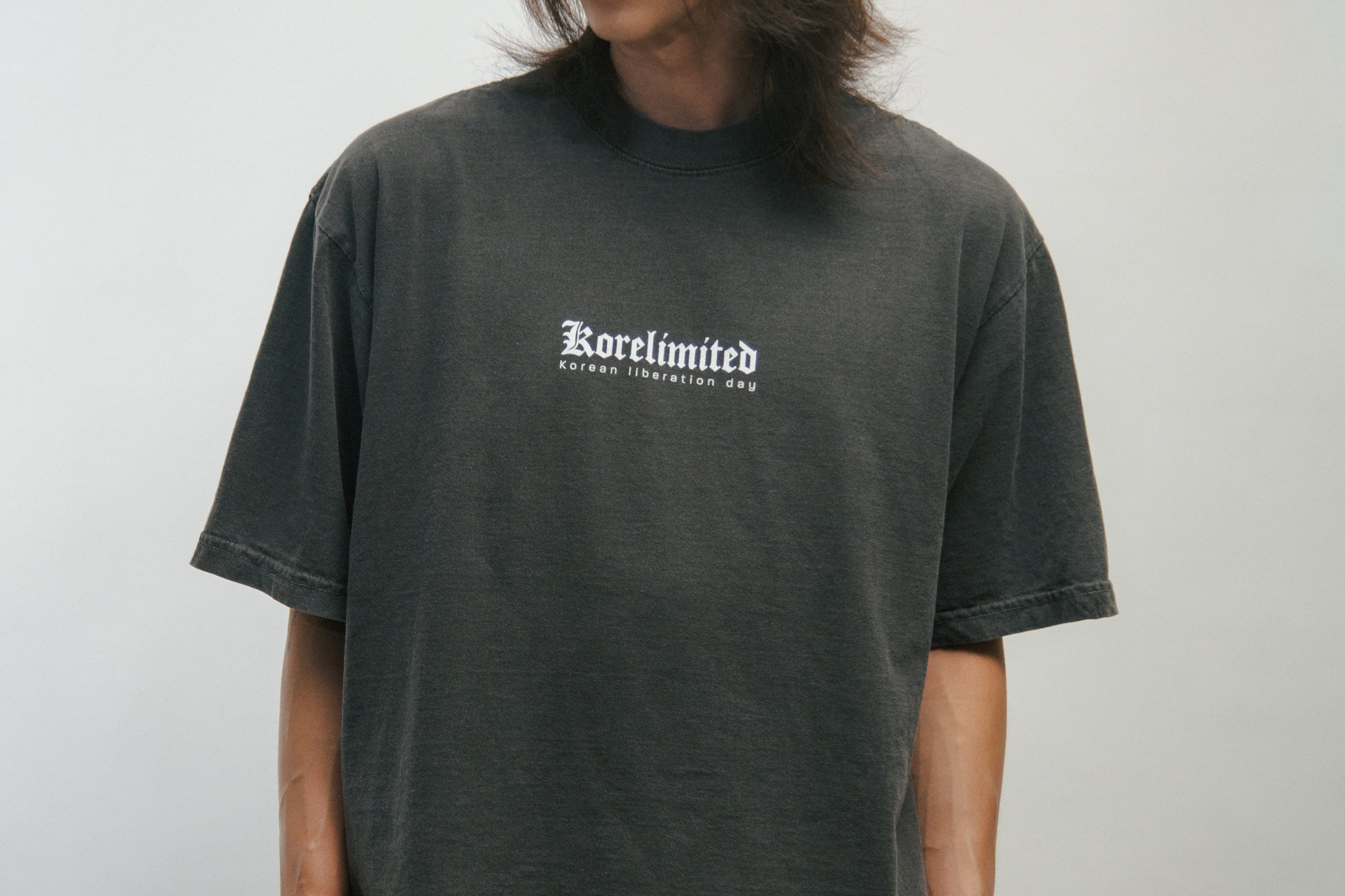 Person wearing a dark gray t-shirt with KORELIMITED text on a plain background