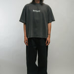 Person wearing a dark t-shirt with text KORELIMITED and black pants on a plain background