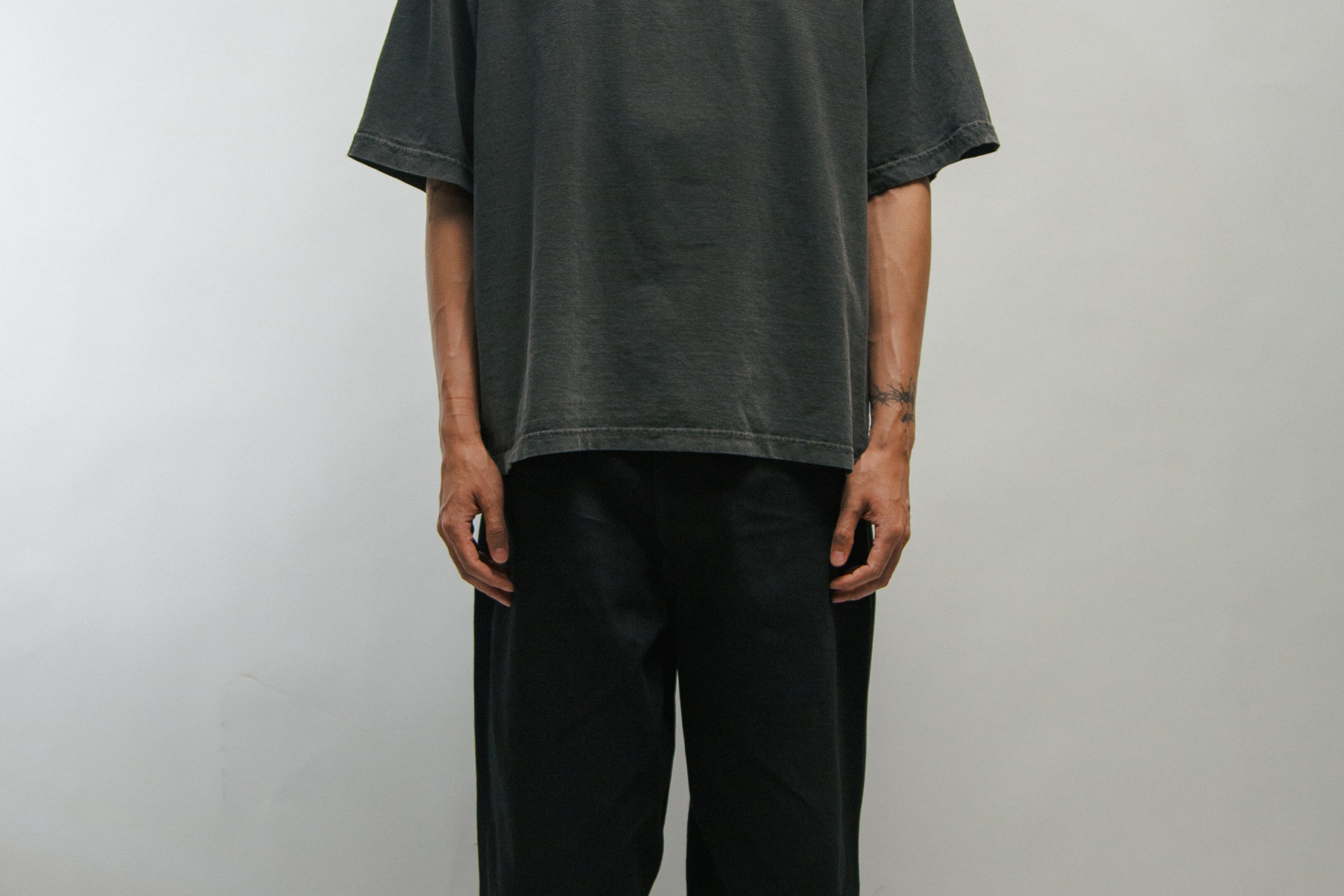Person wearing a dark t-shirt with text KORELIMITED and black pants on a plain background