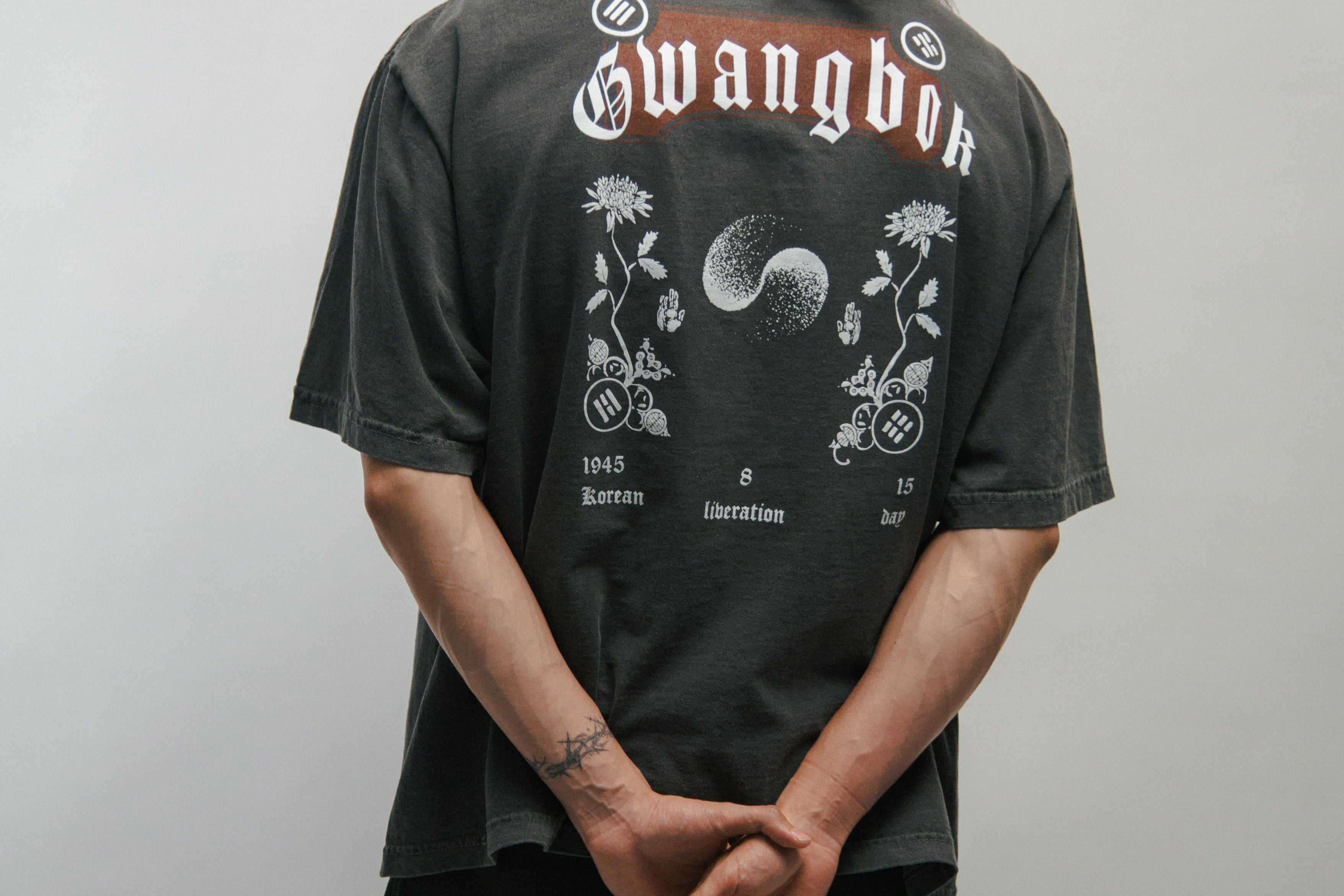 Person wearing a dark grey t-shirt with 'Gwangbok' branding on the back against a plain background