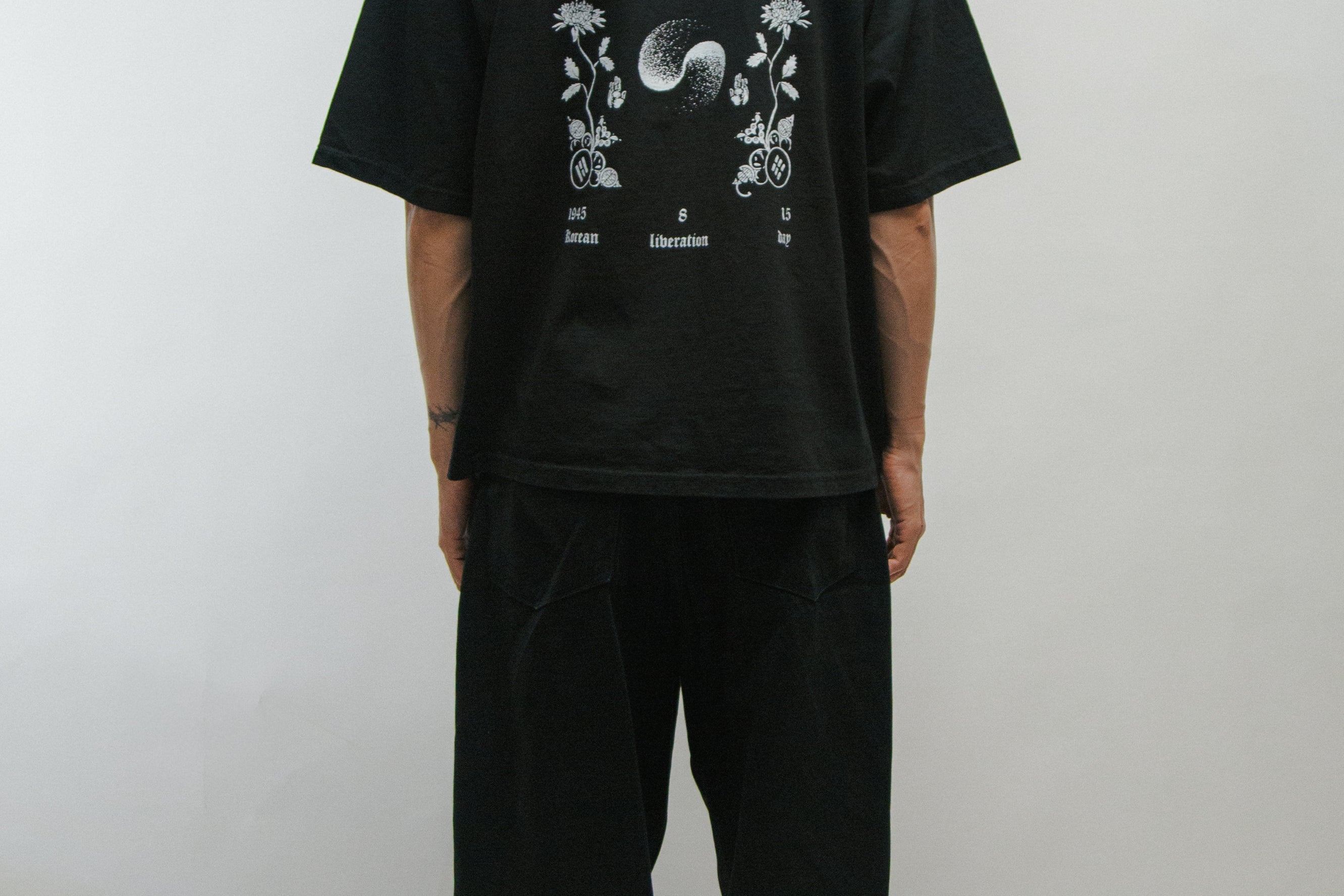 Person wearing a black t-shirt with 'Gwangbok' design on the back against a plain background
