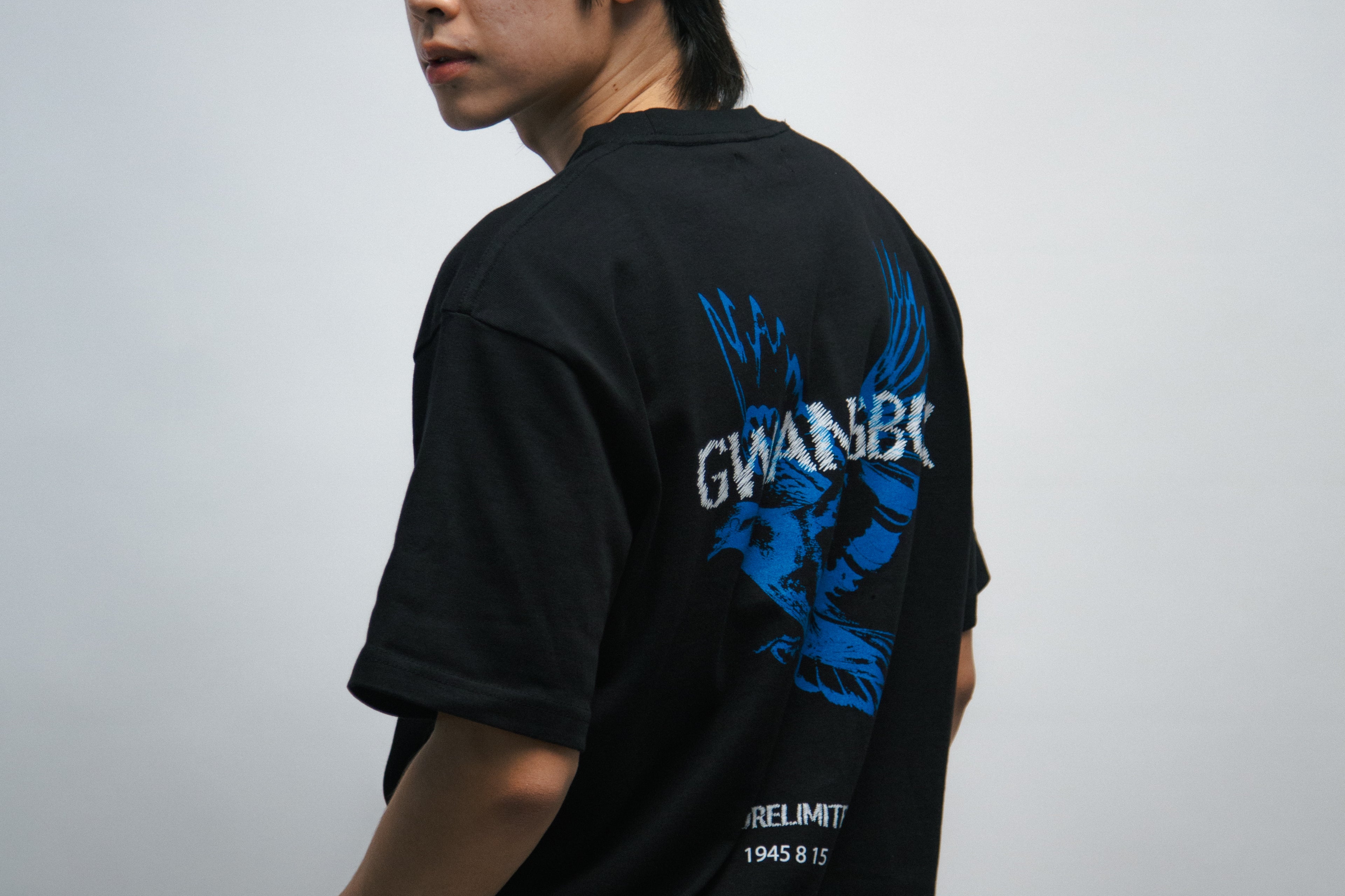 Person wearing a black t-shirt with blue dove bird graphics and white text, standing against a plain background