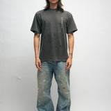 Male person wearing a dark gray t-shirt with Korean characters and blue jeans standing against a plain background