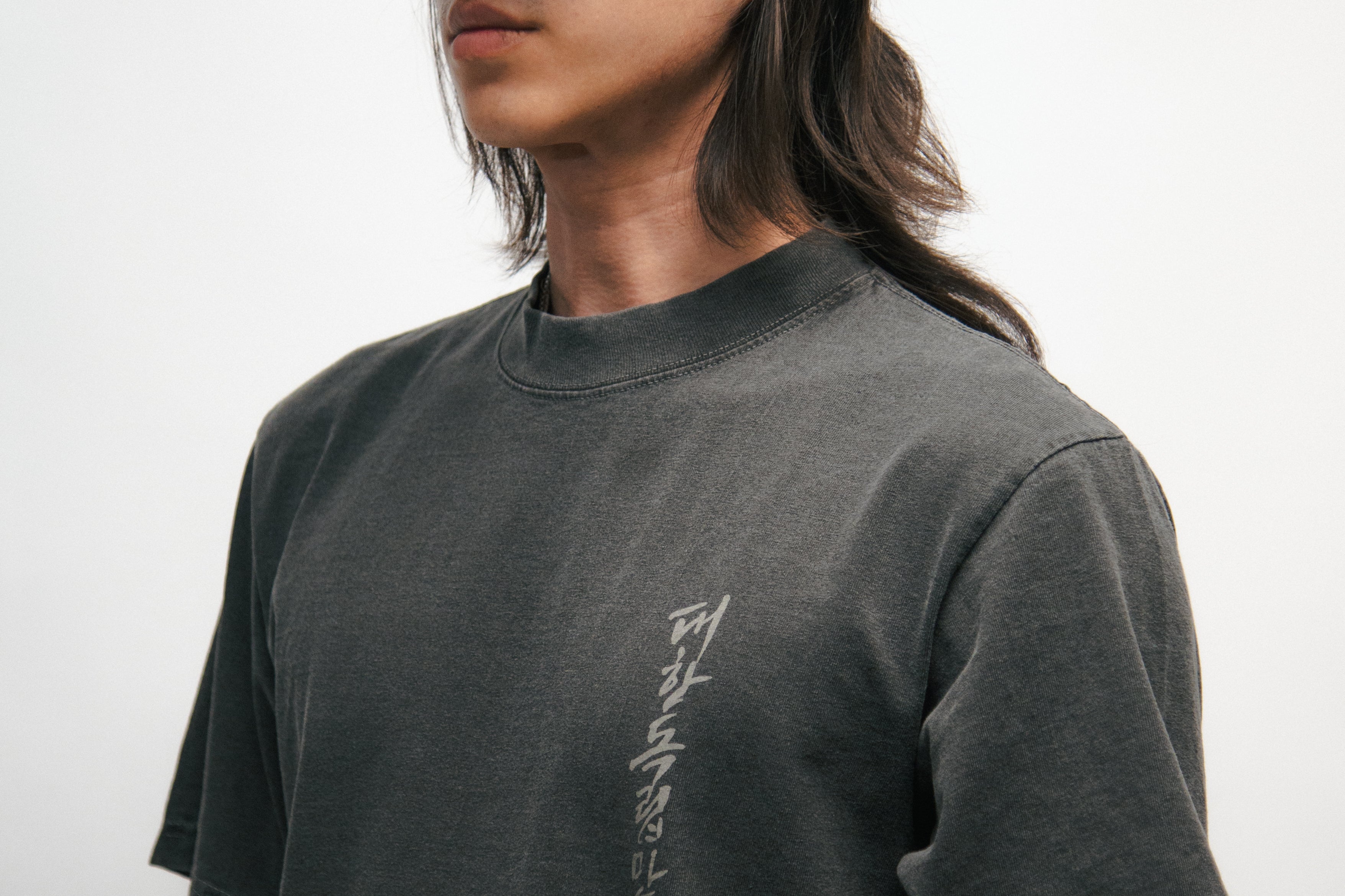 Person wearing a black cap and dark t-shirt with a Korean font logo on a white background