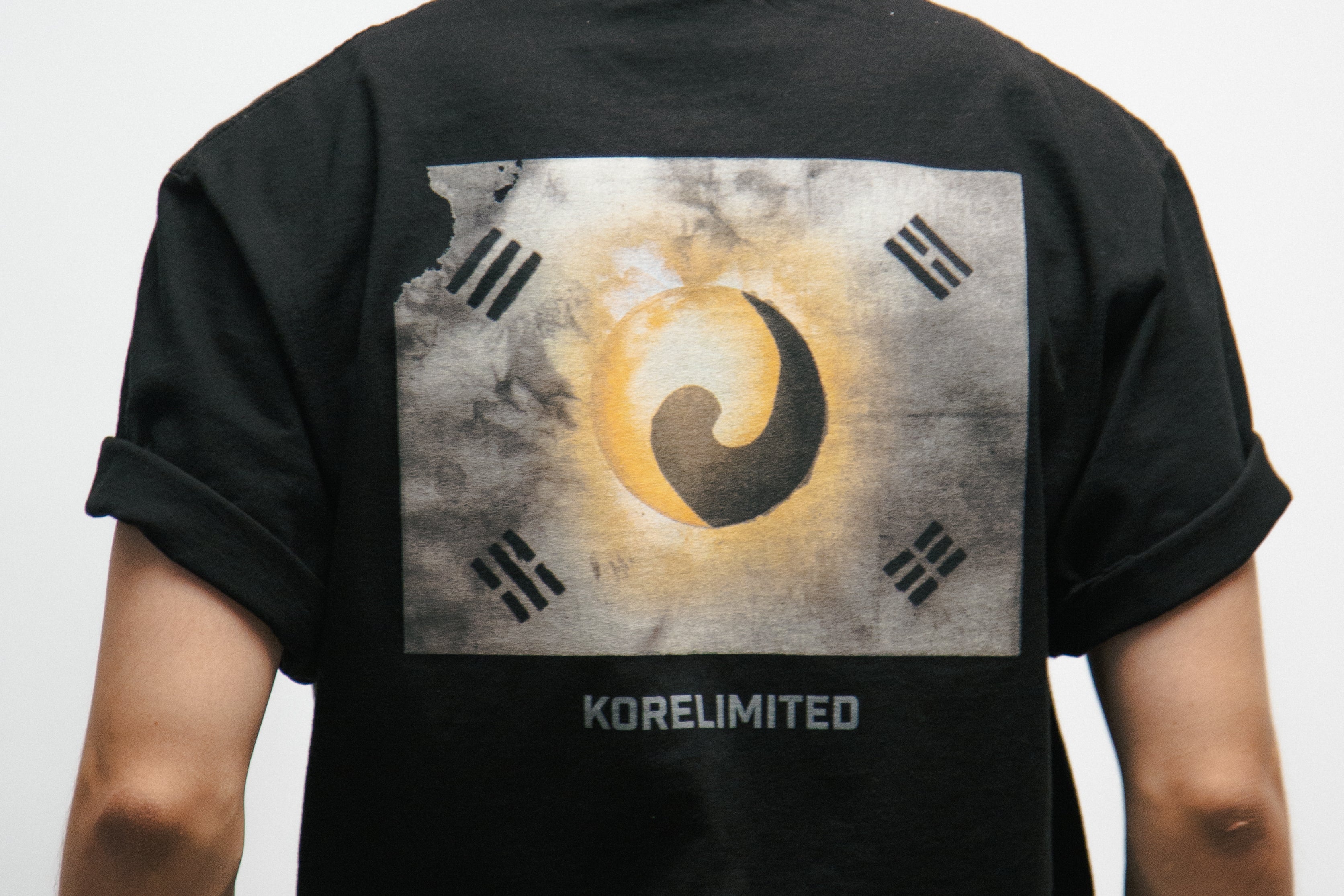 Person wearing a black t-shirt with a design of a vintage Korean Flag on the back, standing against a plain background.