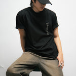 Person wearing a black t-shirt with Korean font on the front and cap with text, sitting against a white background