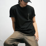 Person wearing a black t-shirt with Korean font on the front and cap with text, sitting against a white background